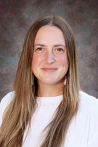 A smiling woman with long brown hair wearing a white shirt, set against a textured gray background.