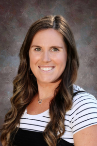 A smiling woman with long, wavy hair, wearing a striped shirt, poses against a textured background.