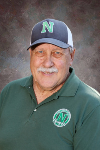Smiling older man wearing a green polo shirt and a cap with an "N" logo, set against a textured background.