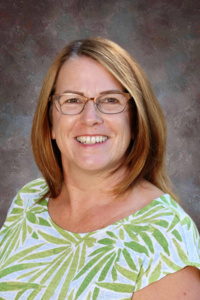 A smiling woman with shoulder-length brown hair, wearing glasses and a green and white patterned shirt.