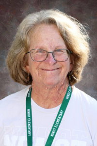 Smiling woman with glasses and curly hair, wearing a white shirt and a green lanyard from a school.